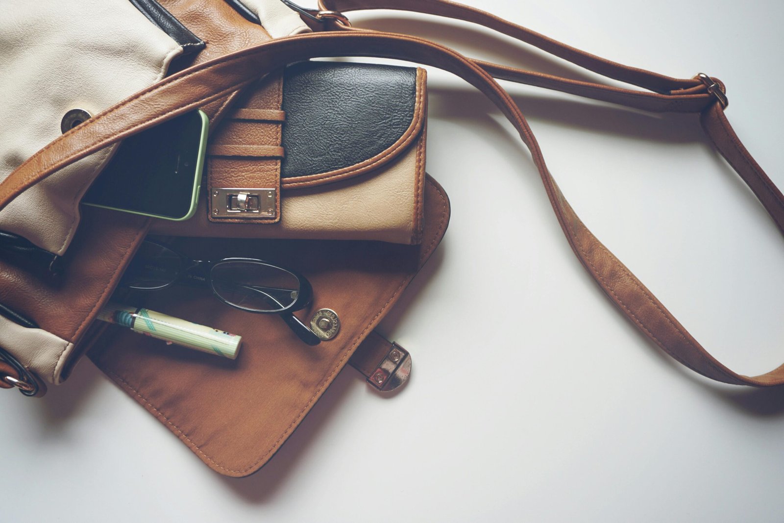 Home Overhead view of leather bag with eyeglasses, wallet, and smartphone laid out.